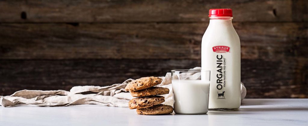 straus organic milk in a glass next to stack of chocolate chip cookies