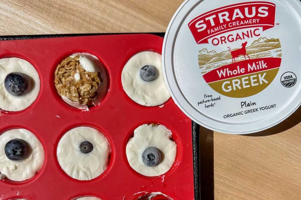 straus whole milk greek plain yogurt next to silicon muffin tray filled with yogurt, blueberries, and granola