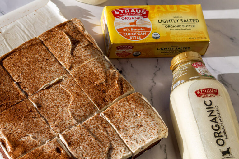 Organic eggnog brownies topped with a dusting of cinnamon, shown alongside Straus Family Creamery lightly salted organic butter and a bottle of Straus Organic Eggnog on a marble surface.