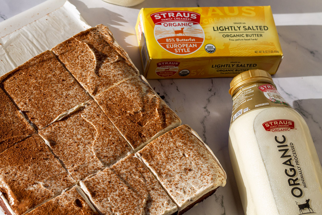 Organic eggnog brownies topped with a dusting of cinnamon, shown alongside Straus Family Creamery lightly salted organic butter and a bottle of Straus Organic Eggnog on a marble surface.