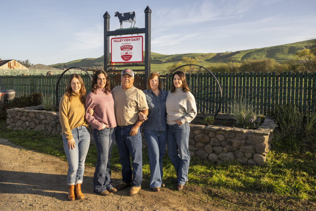 Camozzi family standing together in front of a Valley View Dairy sign with green hills in the background