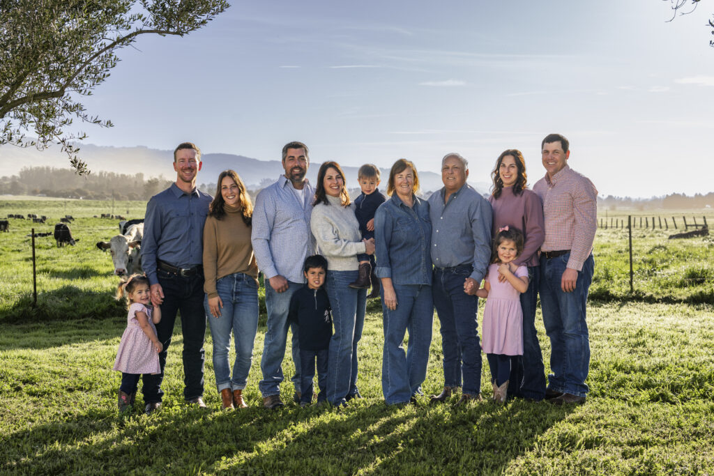 Multi-generational Camozzi family standing together in a pasture with dairy cows behind them
