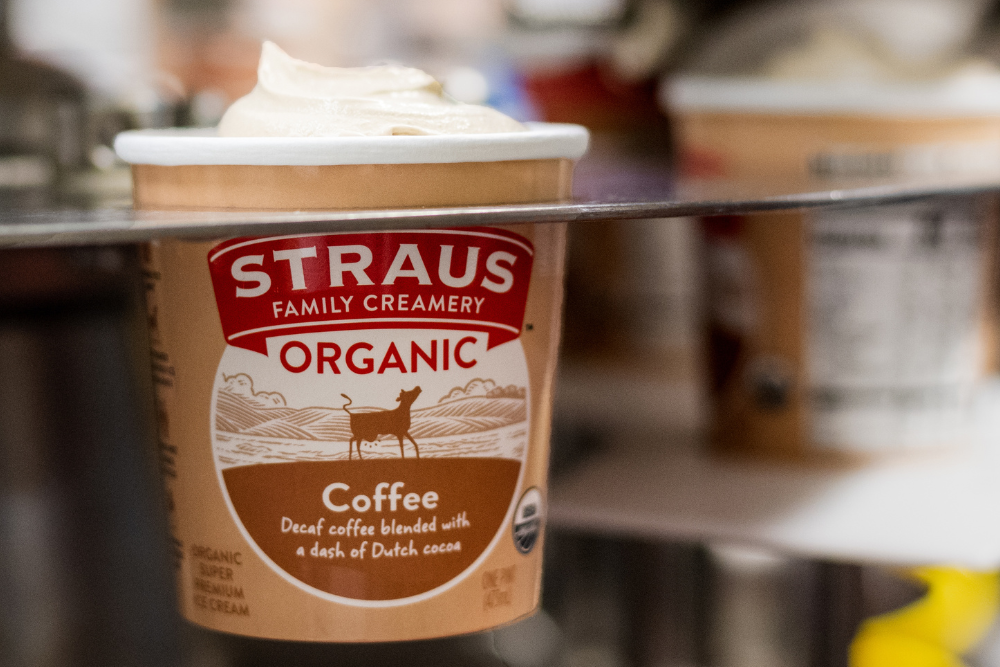 Container of Straus Family Creamery Organic ice cream on a production line, being sealed with a lid in a creamery facility.