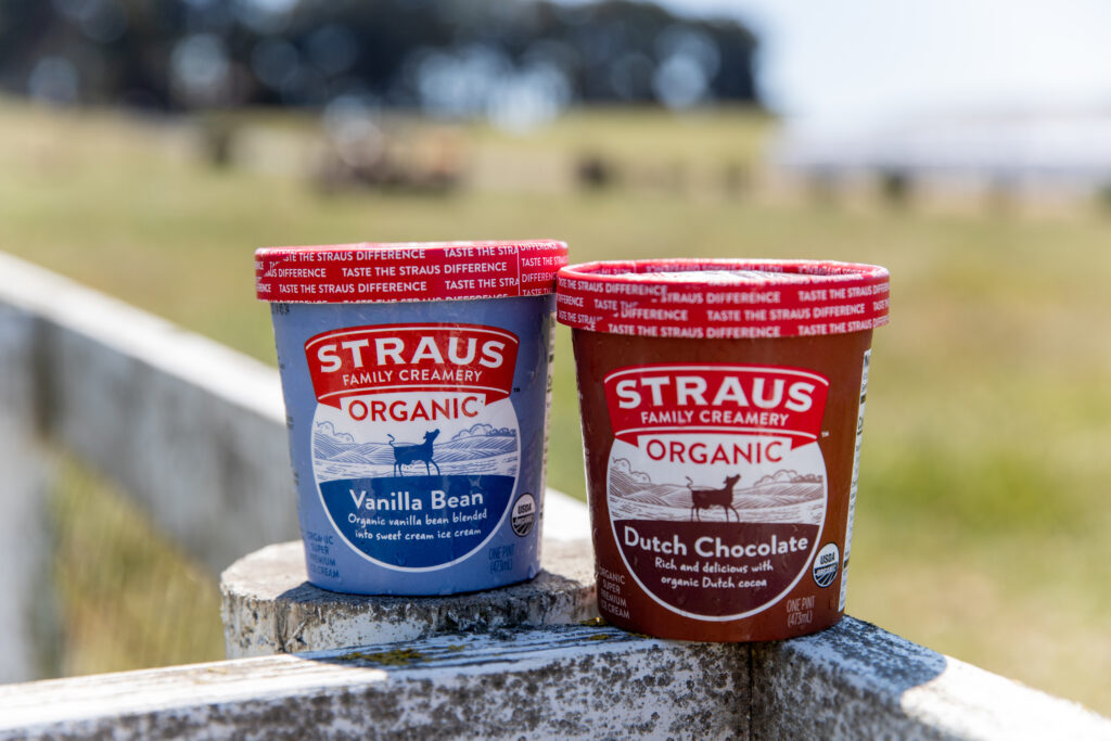 Straus Organic Vanilla Bean and Dutch Chocolate ice cream pints on a farm fence rail with pasture in the background